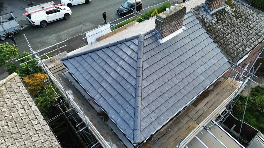 New grey hip roof with scaffold, a chimney and parked vans below
