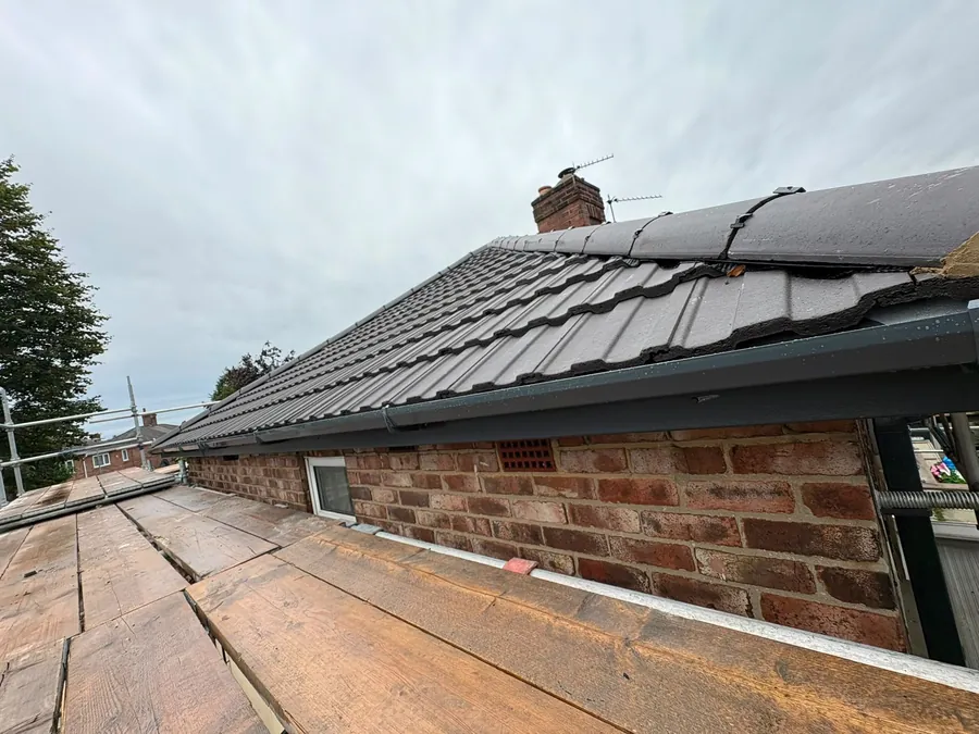 New grey tiles finished at the eaves over a new fascia, seen from the scaffold