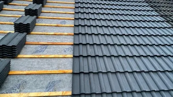 Grey interlocking tiles going on next to tiles stacked on new battens