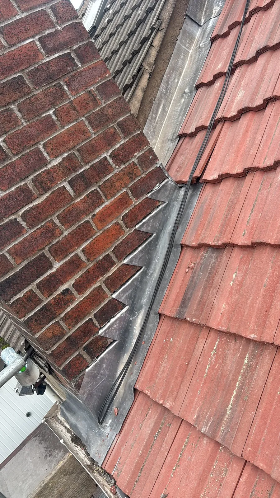 Lead step flashing between red tiles and a chimney