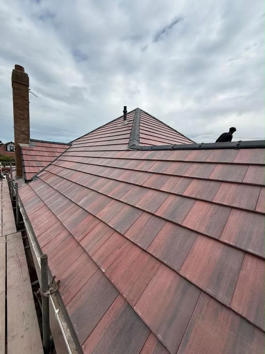Red tile roof with a chimney and a roofer at the ridge